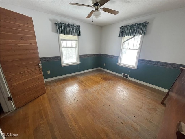 empty room with a wainscoted wall, visible vents, a wealth of natural light, and wood finished floors