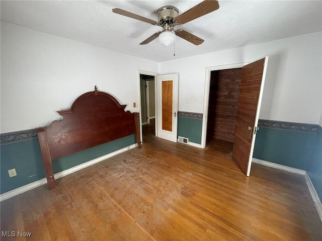 unfurnished bedroom with visible vents, ceiling fan, a textured ceiling, wood finished floors, and baseboards