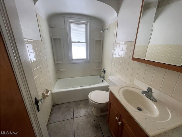 bathroom with toilet, tile patterned flooring, vanity, shower / washtub combination, and tile walls