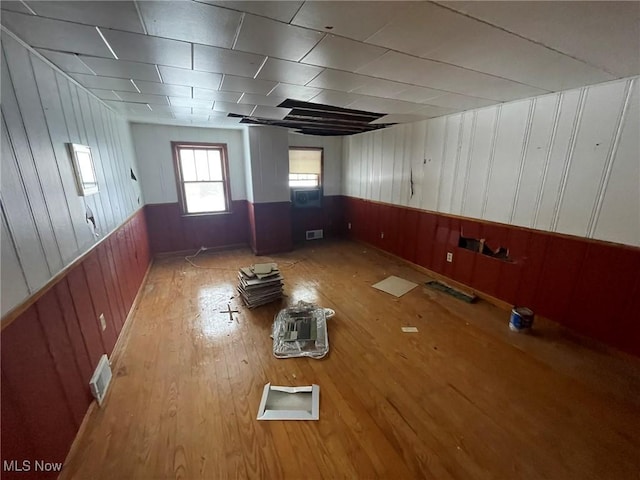 empty room featuring a wainscoted wall, visible vents, wood finished floors, and wood walls