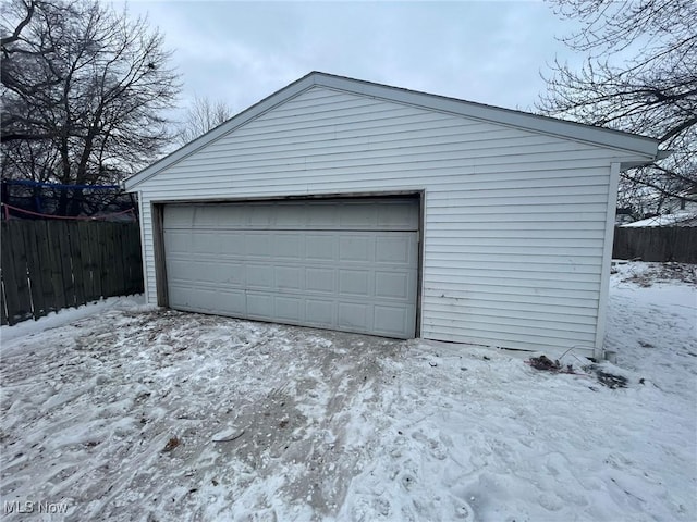 snow covered garage featuring a detached garage and fence