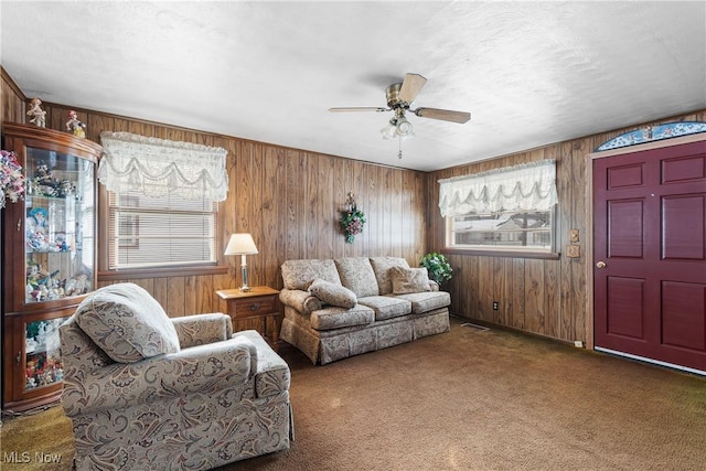 living room featuring dark colored carpet, visible vents, wood walls, a textured ceiling, and ceiling fan