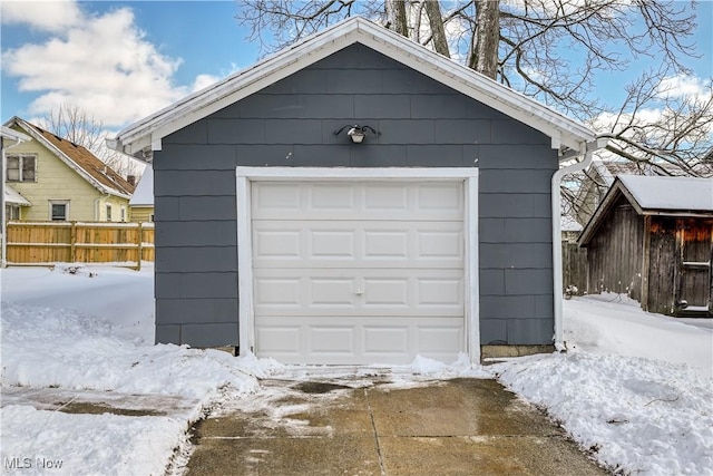 snow covered garage with a garage and fence