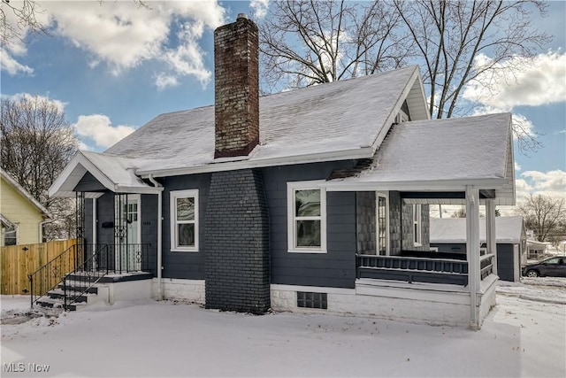 snow covered rear of property featuring a chimney and a porch