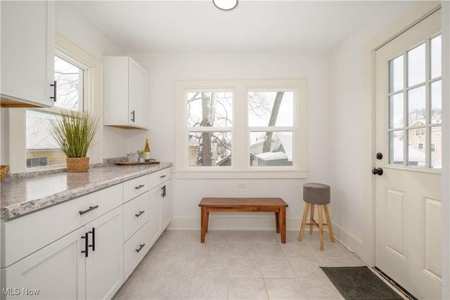 interior space featuring light stone counters, white cabinets, and baseboards