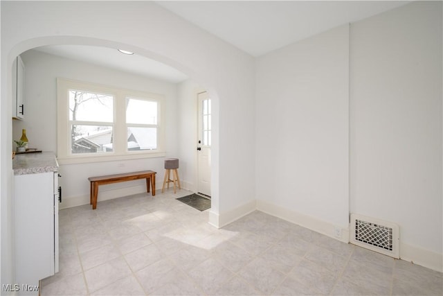 unfurnished room featuring baseboards, visible vents, and arched walkways