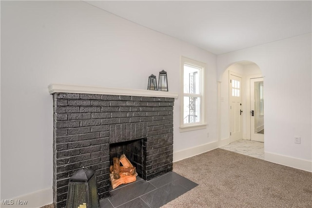 unfurnished living room with baseboards, arched walkways, marble finish floor, carpet flooring, and a fireplace