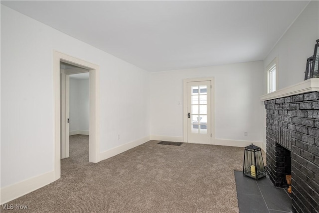 unfurnished living room featuring a brick fireplace, dark carpet, and baseboards