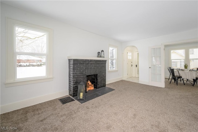 living area featuring arched walkways, carpet flooring, visible vents, baseboards, and a brick fireplace