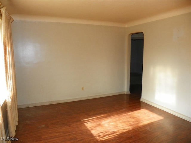 spare room featuring arched walkways, dark wood finished floors, and baseboards