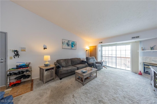 living area featuring high vaulted ceiling, a tiled fireplace, visible vents, and light colored carpet