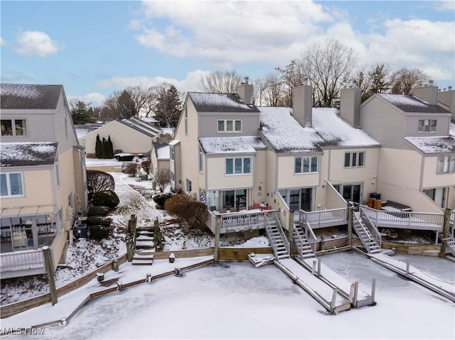 snow covered property featuring a residential view, a chimney, stairway, and a wooden deck