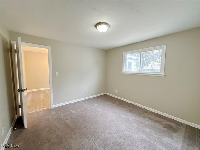 spare room featuring dark colored carpet and baseboards