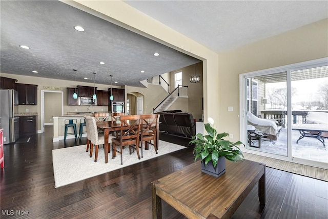 dining room featuring arched walkways, a textured ceiling, recessed lighting, dark wood-style flooring, and stairway