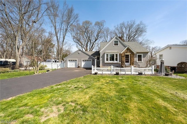 view of front of house with driveway, a garage, stone siding, a fenced front yard, and a front yard