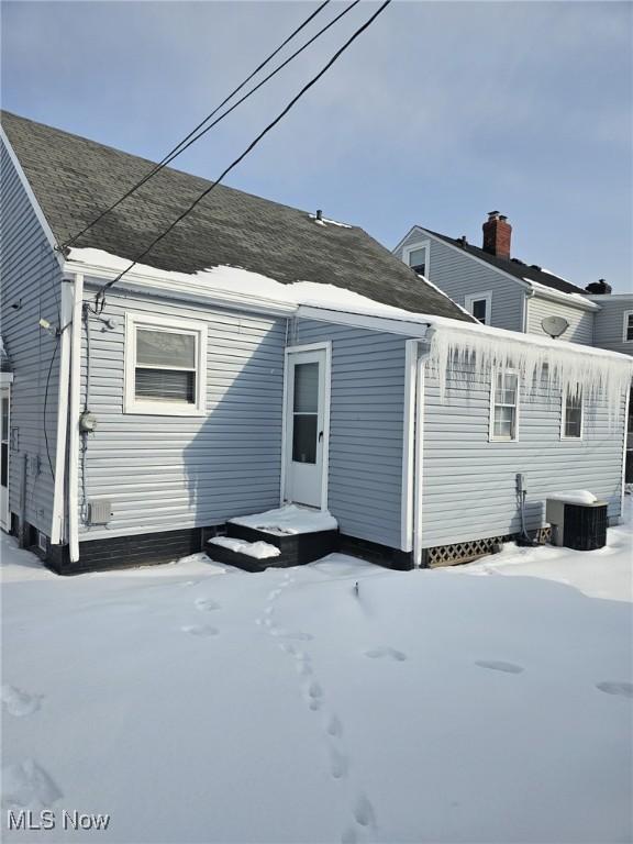 snow covered property with central AC unit and roof with shingles