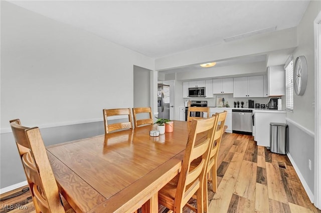 dining space featuring light wood finished floors, visible vents, and baseboards