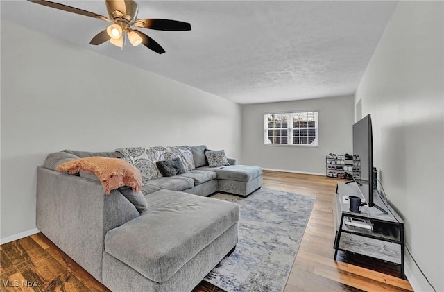 living room featuring a textured ceiling, ceiling fan, light wood finished floors, and baseboards