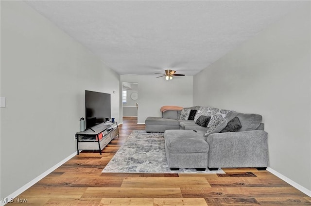 living room featuring a ceiling fan, baseboards, and wood finished floors