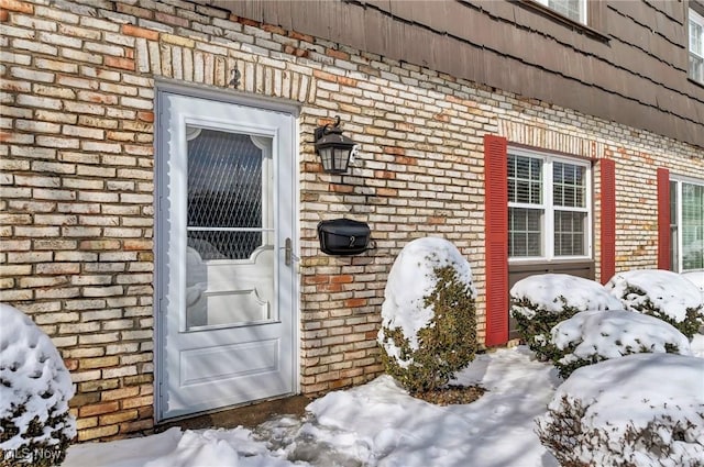 snow covered property entrance featuring brick siding