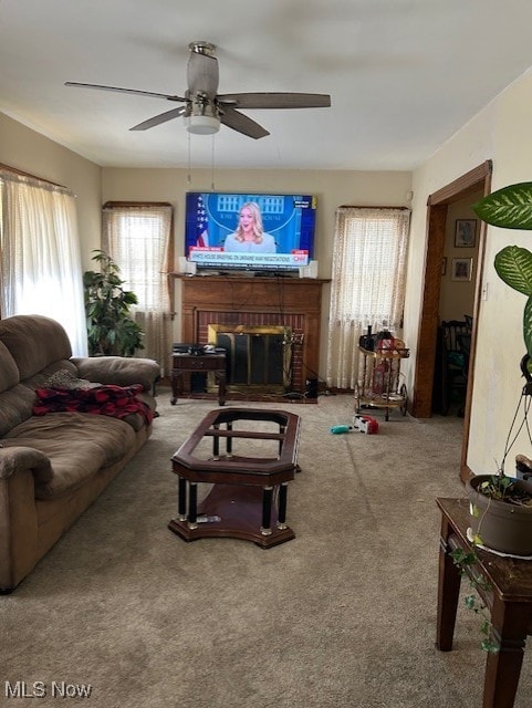 living area with a brick fireplace, carpet flooring, and a ceiling fan