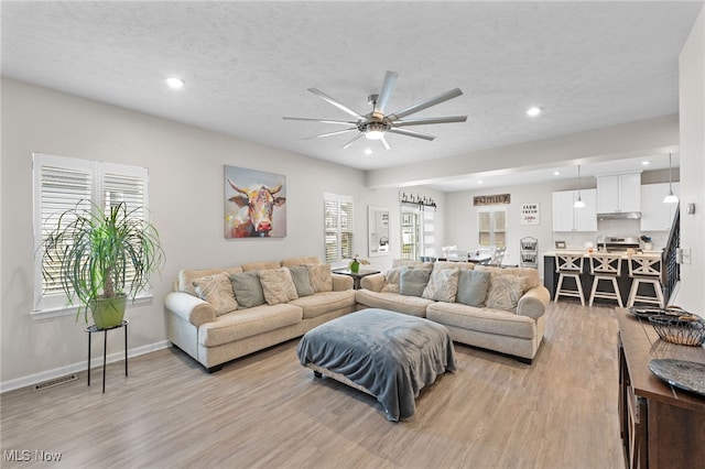 living room featuring a textured ceiling, light wood-type flooring, baseboards, and recessed lighting