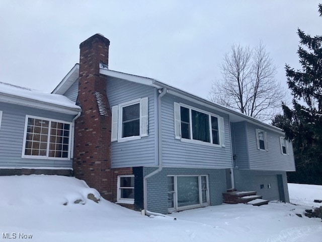 view of snowy exterior featuring a garage, a chimney, and brick siding