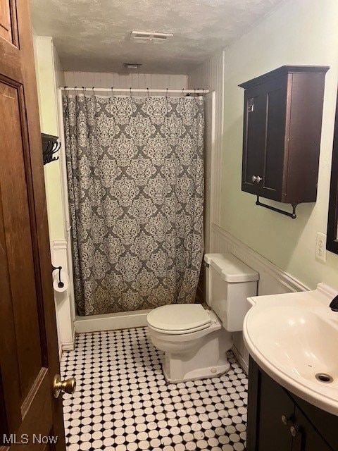 full bathroom featuring visible vents, toilet, vanity, a textured ceiling, and baseboards