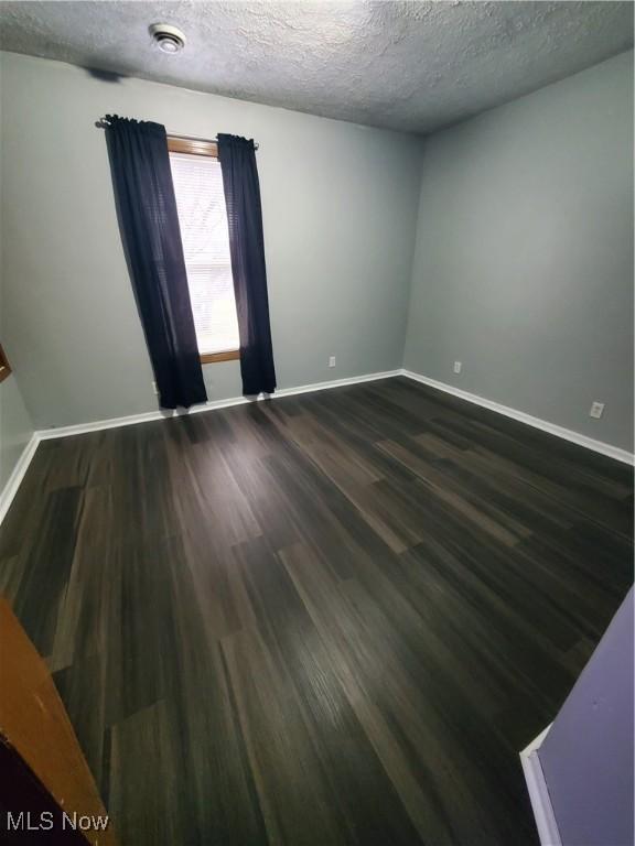 unfurnished room with a textured ceiling, dark wood-type flooring, and baseboards