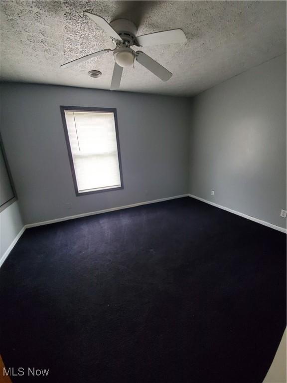 empty room with dark carpet, ceiling fan, a textured ceiling, and baseboards