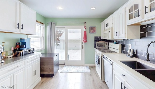 kitchen with white appliances, a sink, glass insert cabinets, and white cabinets