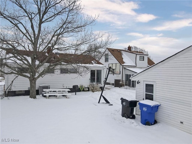 snow covered property with entry steps, a garage, a chimney, and central AC unit