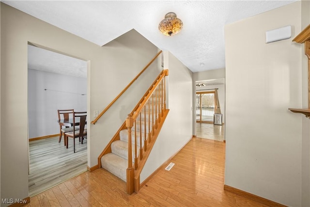 stairs featuring a textured ceiling, wood finished floors, visible vents, and baseboards