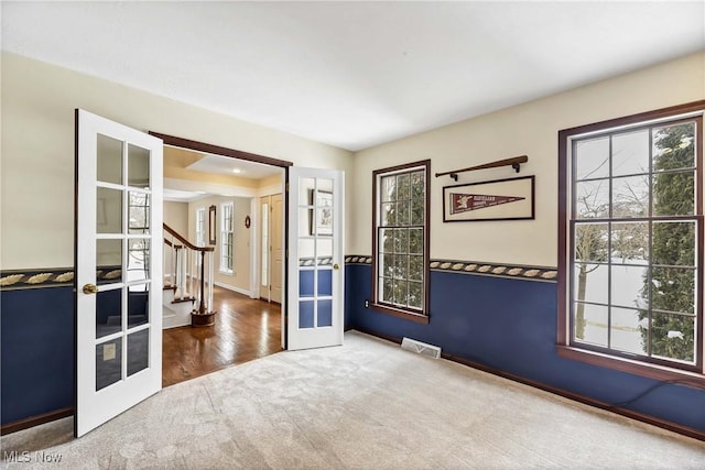 carpeted empty room featuring french doors, visible vents, baseboards, and stairs