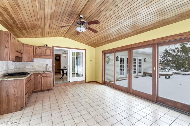 kitchen with lofted ceiling, backsplash, brown cabinetry, and a sink