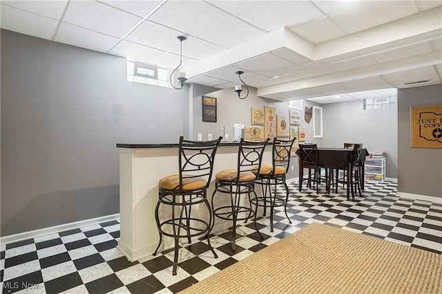 bar with dark floors, indoor wet bar, a paneled ceiling, and baseboards