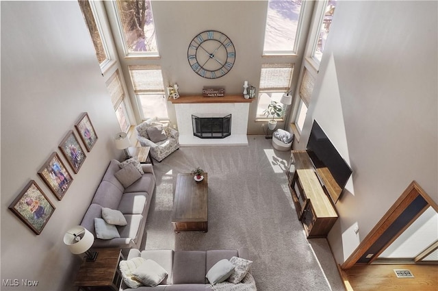 living room featuring a towering ceiling, a brick fireplace, plenty of natural light, and carpet flooring