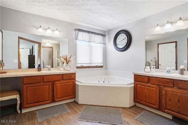 full bath with a textured ceiling, two vanities, a bath, and wood finished floors