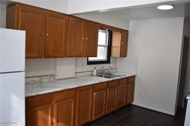 kitchen featuring tasteful backsplash, brown cabinetry, dark wood-style floors, freestanding refrigerator, and a sink