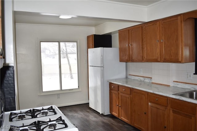 kitchen with dark wood-style flooring, brown cabinets, decorative backsplash, freestanding refrigerator, and a sink