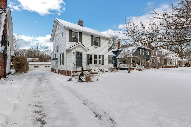 snow covered house featuring entry steps, a detached garage, and a chimney