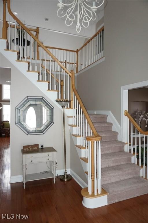 stairs with a notable chandelier, a high ceiling, baseboards, and wood finished floors