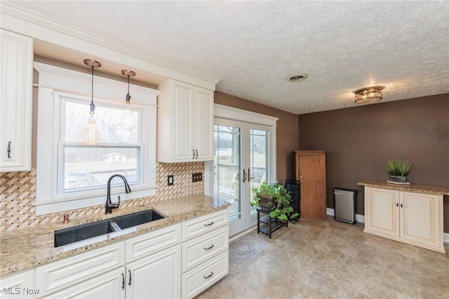 kitchen featuring hanging light fixtures, light stone counters, white cabinets, and a sink