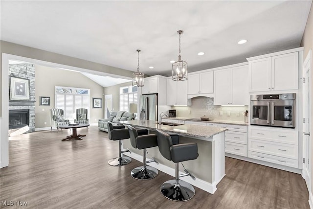 kitchen with a center island with sink, white cabinets, light stone countertops, stainless steel appliances, and a sink