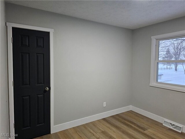 unfurnished room featuring light wood-style flooring, a textured ceiling, visible vents, and baseboards