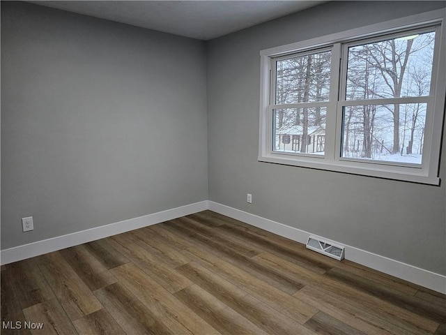 spare room featuring baseboards, visible vents, and wood finished floors