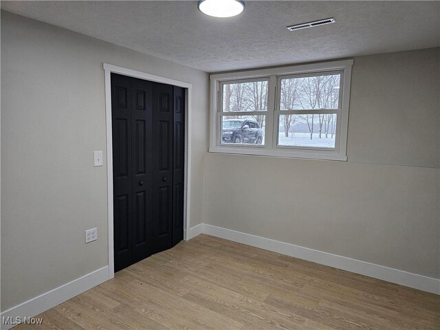 unfurnished bedroom featuring a textured ceiling, visible vents, baseboards, a closet, and light wood-type flooring