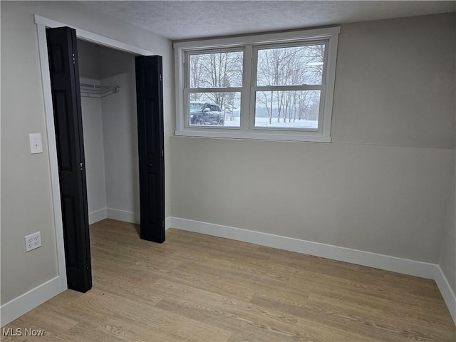 unfurnished bedroom featuring light wood-type flooring, a closet, a textured ceiling, and baseboards