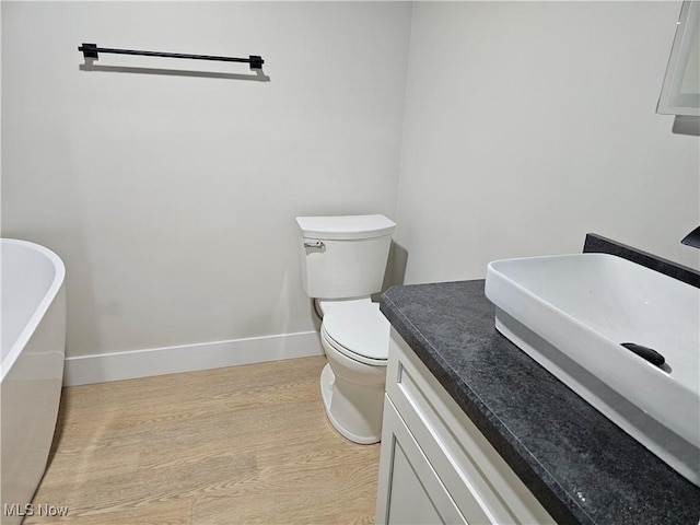 bathroom with toilet, wood finished floors, vanity, baseboards, and a soaking tub