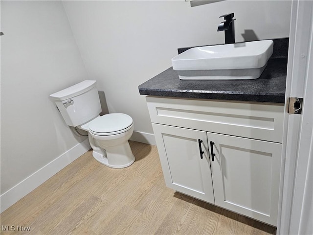 half bathroom with toilet, baseboards, wood finished floors, and vanity